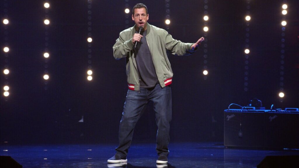 Adam Sandler performing on Stage, Symbolizing his success and wealth in the entertainment industry