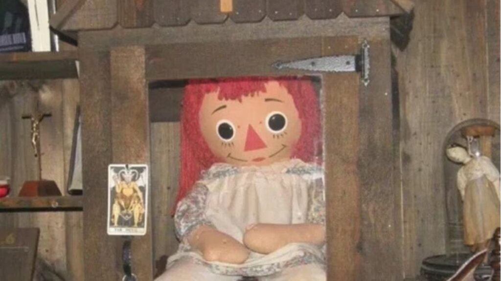 The Annabelle doll displayed inside a haunted house setting, surrounded by dim lighting and eerie vintage decor