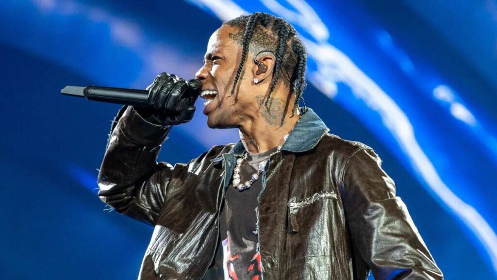 Travis Scott standing in front of a crowd during a live performance, surrounded by Cactus Jack branding and fiery stage visuals, capturing the immersive spectacle and marketing frenzy of his hype machine.