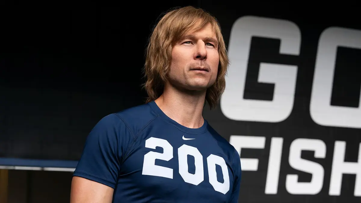 Chad Powers posing on the football field after tryouts, sunlight highlighting his fake hair and confident smirk.