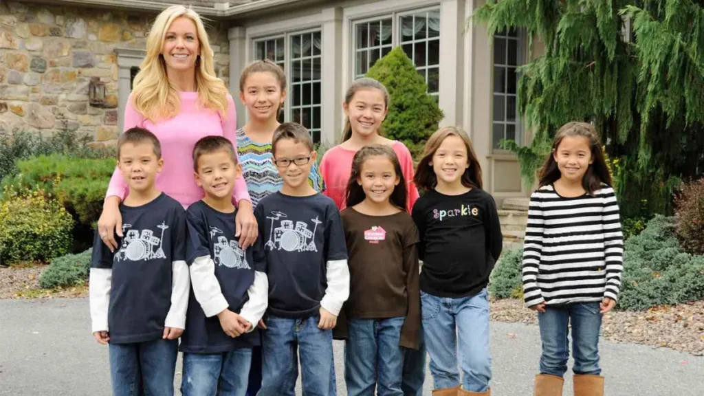 Kate Gosselin posing with her eight children outdoors, all smiling at the camera in coordinated casual outfits.