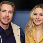 Kristen Bell and Dax Shepard standing together on set, smiling at the camera, promoting their latest project.