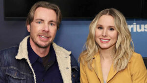 Kristen Bell and Dax Shepard standing together on set, smiling at the camera, promoting their latest project.