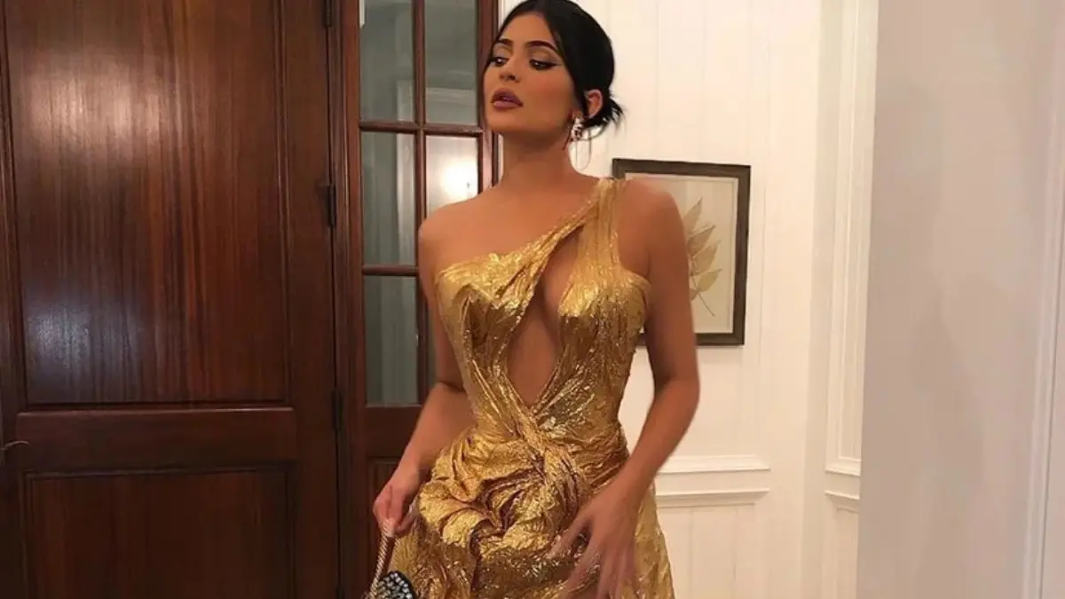 Kylie Jenner posing on the red carpet in a shimmering gold gown, fitted silhouette with a dramatic train and sleek hairstyle.