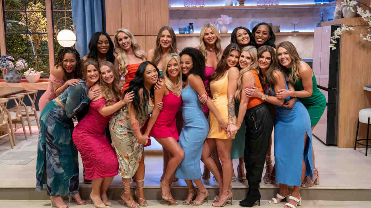 Cast of Love Is Blind standing together on set, dressed in formal attire, smiling in front of the show’s signature glowing pods backdrop.