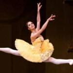 Ballet dancer Misty Copeland mid-leap during her final performance, both legs extended gracefully in the air, arms outstretched under stage lighting.