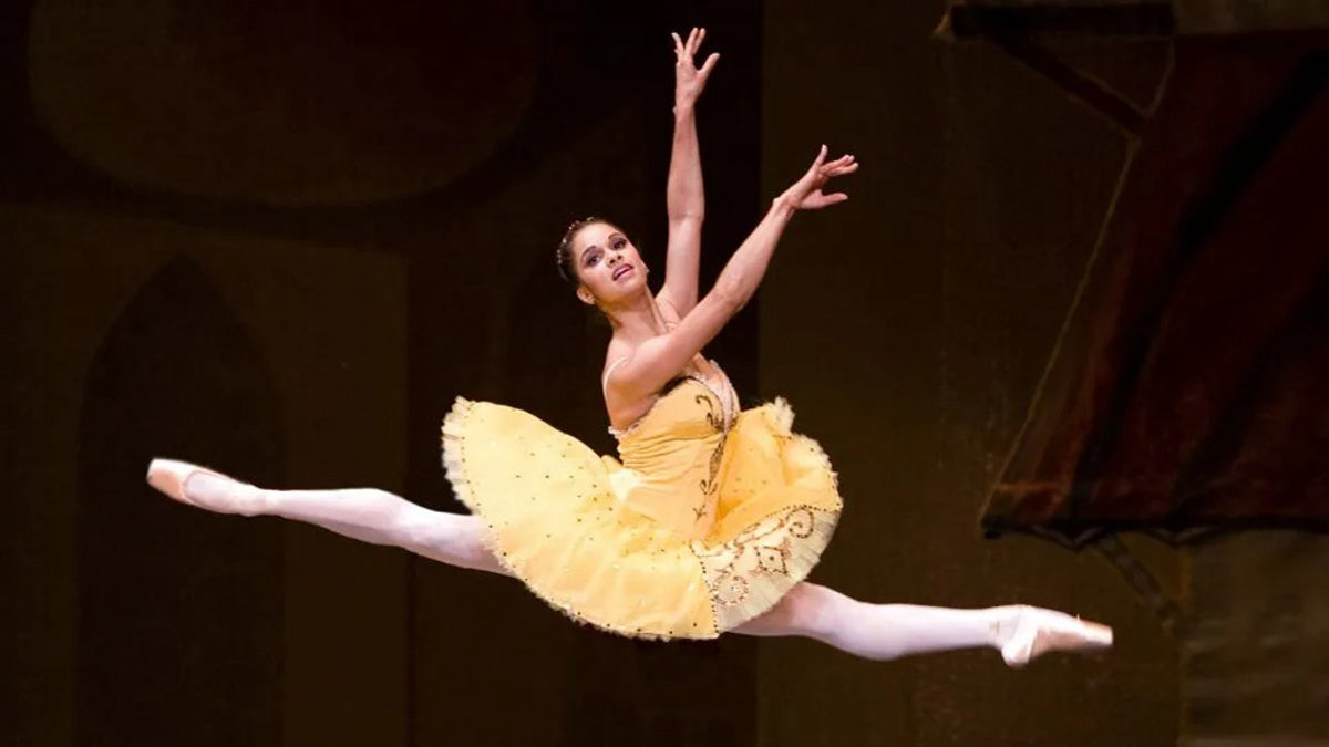 Ballet dancer Misty Copeland mid-leap during her final performance, both legs extended gracefully in the air, arms outstretched under stage lighting.