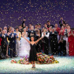 Misty Copeland standing on stage with her family, all smiling and posing together after her performance, with applause from the audience in the background.