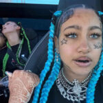 North West displaying playful tattoo designs on her face — a small star under her right eye and her name in cursive script on her left cheek, paired with bold braids and colored contact lenses.